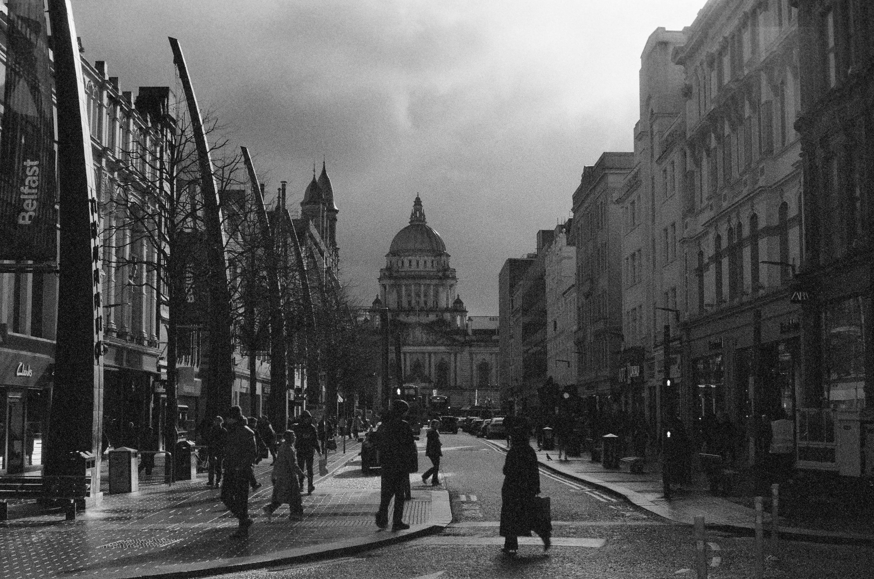 Belfast with people walking, buildings lining the sides, and City Hall in the distance.