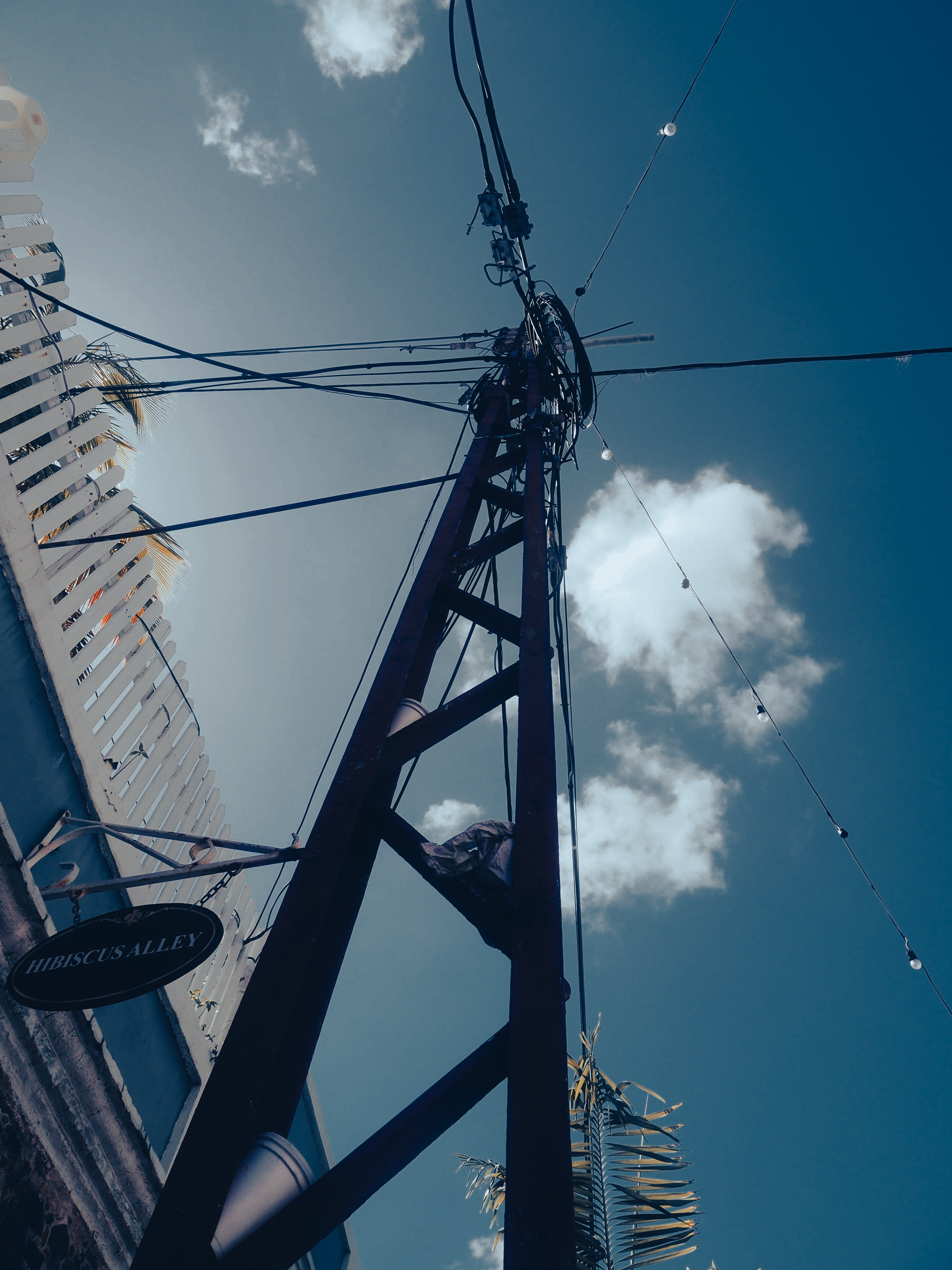 Tall metal pole with electrical wires against a blue sky with clouds